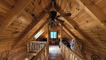 An attic bedroom with a wooden ceiling, a ceiling fan, a bed, and a window.