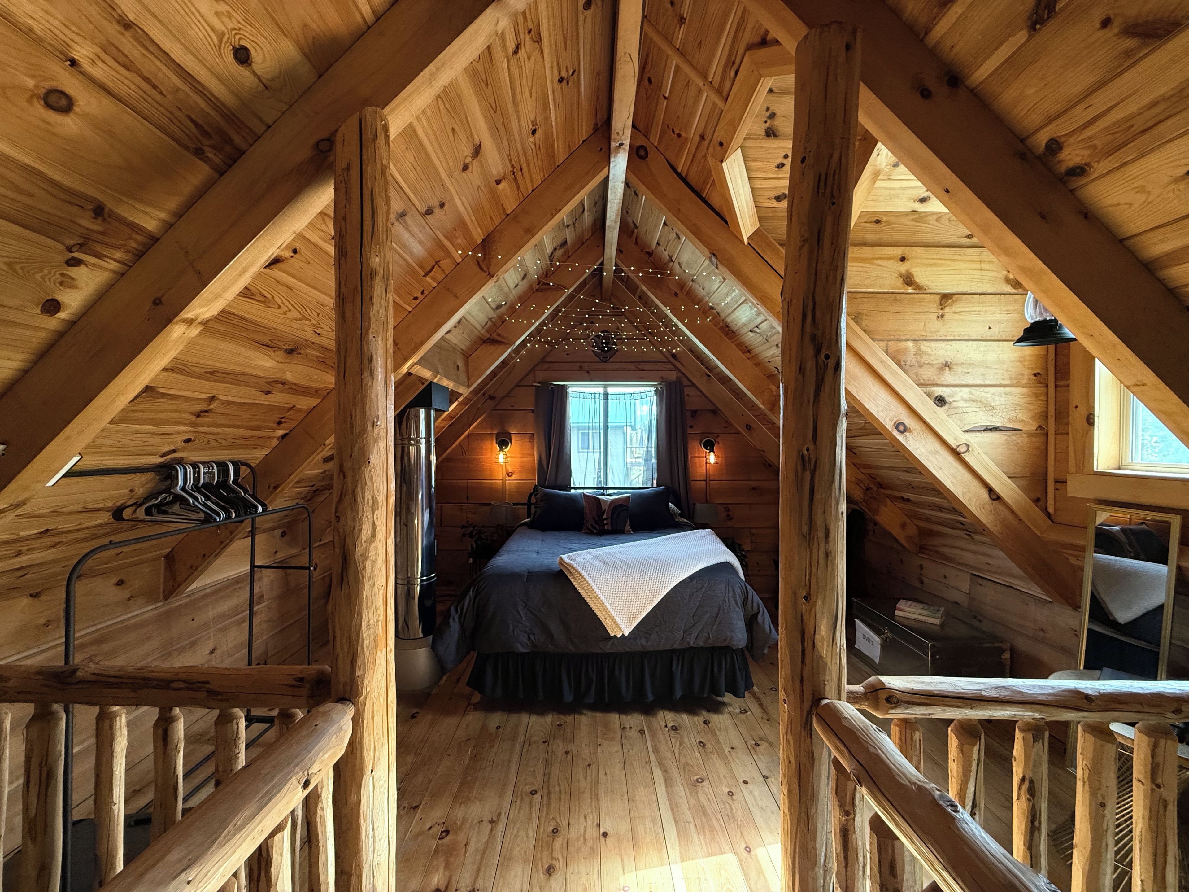 A wooden attic bedroom with a bed, a window, and a staircase.