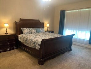 Une chambre à coucher avec un lit en bois, deux tables de chevet, une commode et une fenêtre avec des rideaux.
