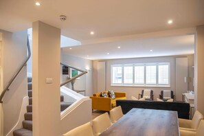 Un salon moderne avec un escalier, un coin repas et une grande fenêtre équipée de stores.
