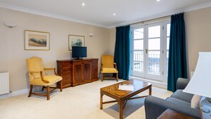 Uma sala de estar ampla com uma mesa de centro de madeira, duas poltronas, um sofá, uma televisão e um armário.