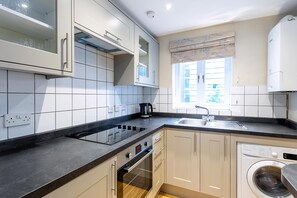 A modern kitchen with white cabinets, a black countertop, a built-in oven, a washing machine, and a window with a curtain.