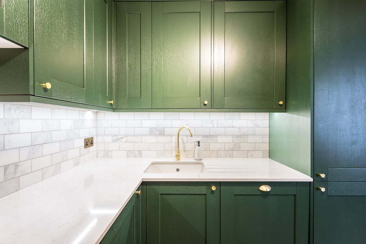A kitchen with green cabinets, a white countertop, and a sink.