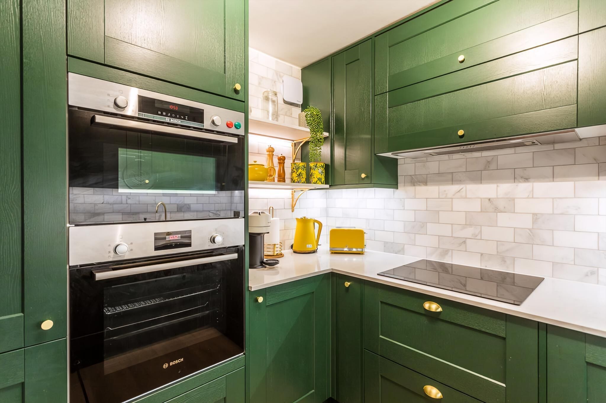 Een keuken met groene kastjes, een Bosch oven, een wit aanrecht en een geel apparaat.
