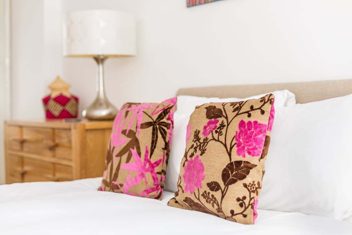 A bed with white sheets and two decorative pillows with floral patterns.