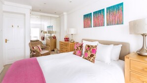 A hotel room with a bed, a nightstand, a lamp, a dresser, a chair, and artwork on the wall.