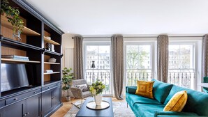 A modern living room with a dark wood bookshelf, a teal sofa with yellow cushions, and a coffee table with a vase.
