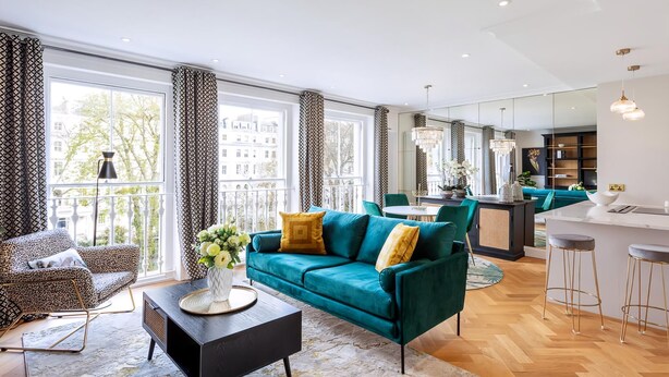 A modern living room with a teal sofa, a black coffee table, and a large window with patterned curtains.