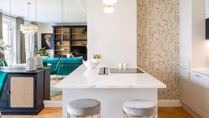 A modern kitchen with a marble island, pendant lighting, and a floral wallpaper accent wall.