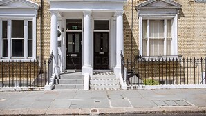A building with a classic facade, featuring a central entrance with white columns and a black door marked with the number 78. - Stunning Earls Court Flat (London)