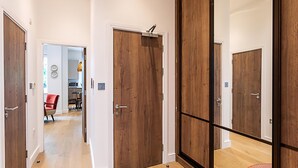 A hallway with wooden doors, a red chair, and a dining area in the background. - Stunning Earls Court Flat (London)
