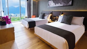 Habitación de hotel con dos camas, un ventanal amplio con vista a la ciudad, una obra de arte colgada en la pared y suelo de madera.