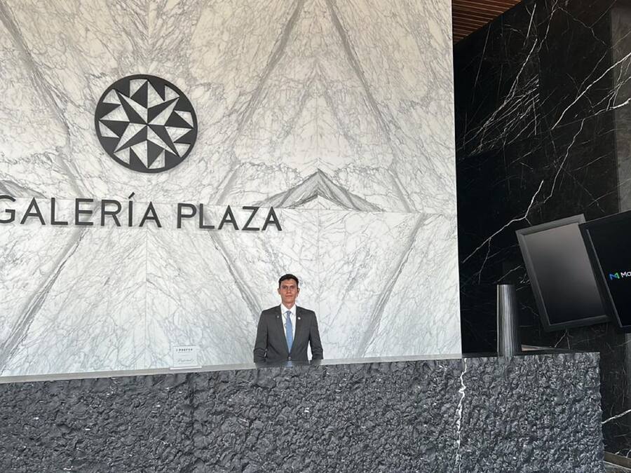 Un hombre de pie frente a un letrero de Galeria Plaza, con una pared de mármol y un piso de mármol negro.