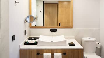 Un baño moderno con lavamanos blanco, tocador de madera, un espejo y un inodoro.