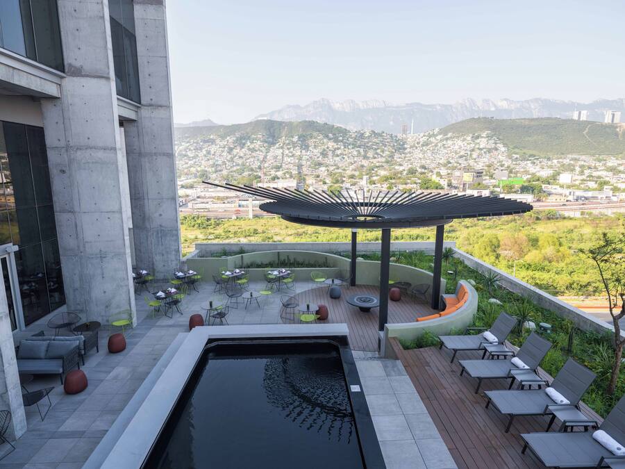 Een dakterras met een zwembad, lounge stoelen en een pergola met uitzicht op een stadslandschap en bergen.