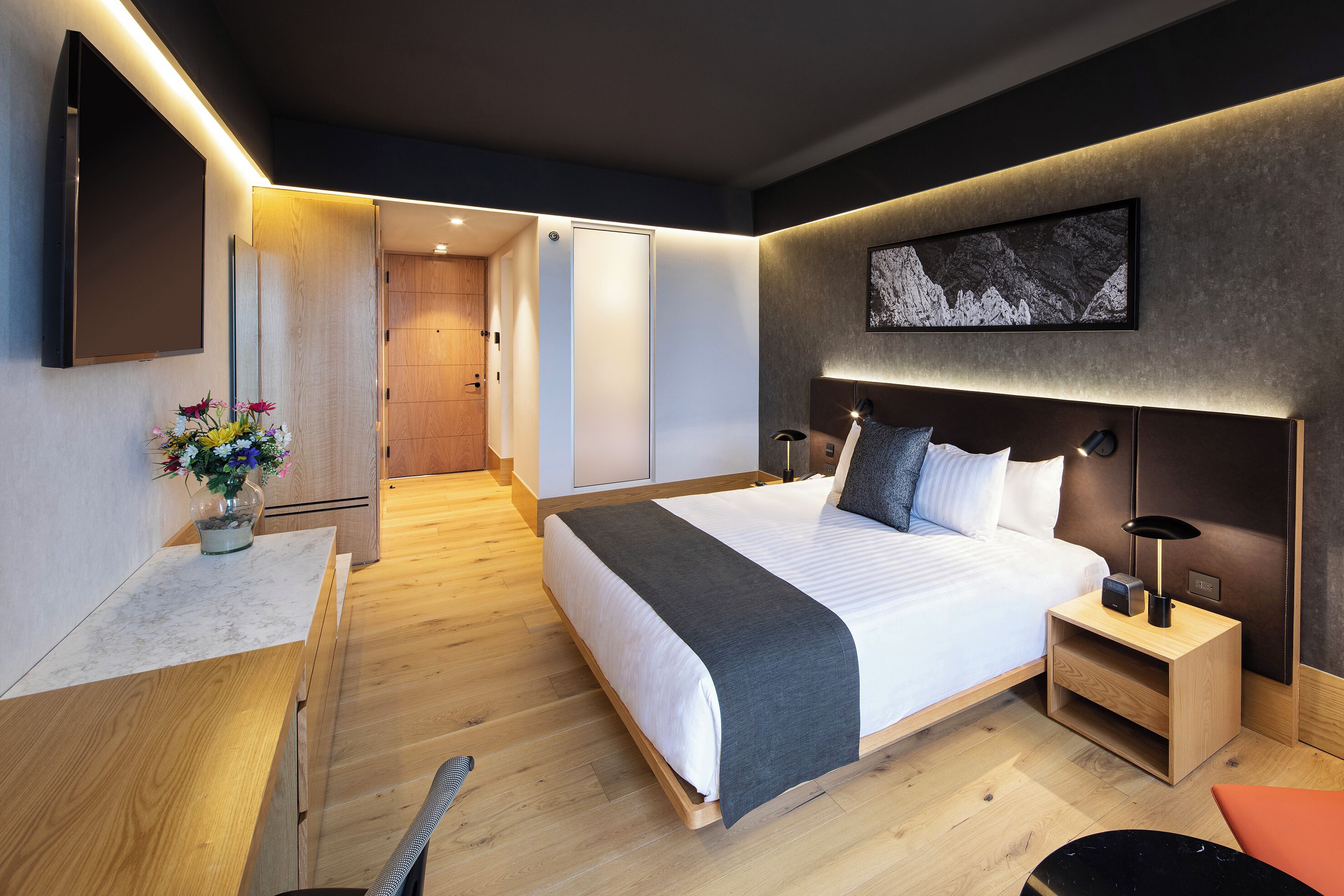 Una habitación de hotel moderna con una cama grande, mesitas de noche, un escritorio y una silla.