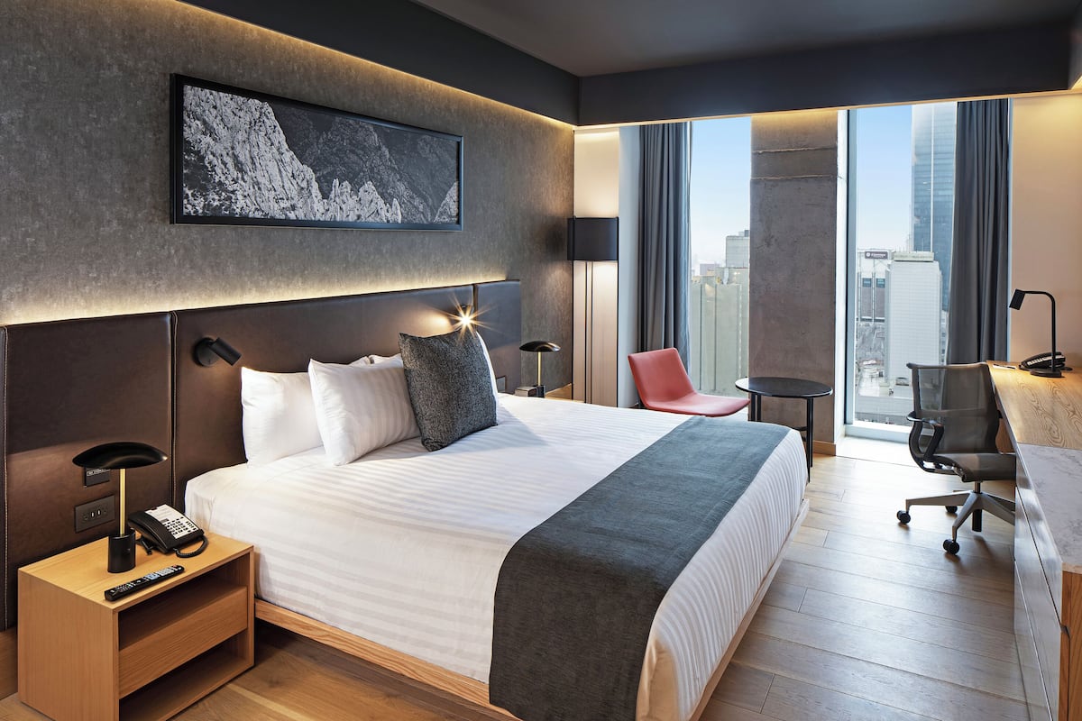 Une chambre d’hôtel moderne, dotée d’un grand lit, d’un bureau, d’une chaise et offrant une vue sur la ville.