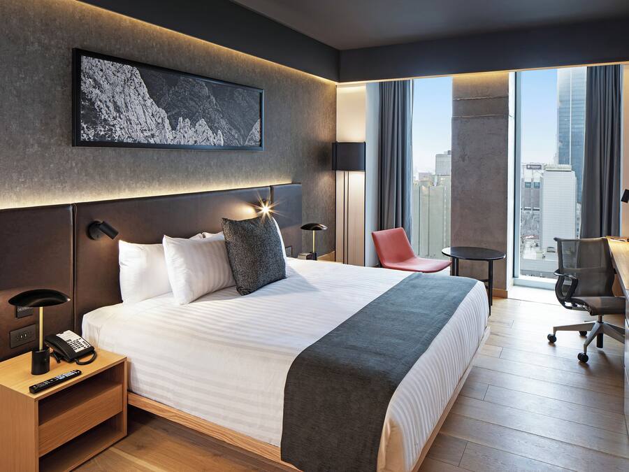 Ett modernt hotellrum med en stor säng, ett skrivbord, en stol och utsikt över staden.