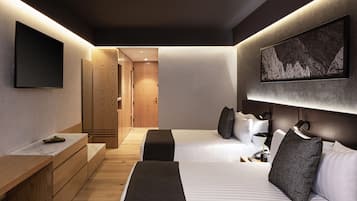 A modern hotel room with two beds, a flat-screen TV mounted on the wall, a wooden desk, and a large framed picture above the bed.