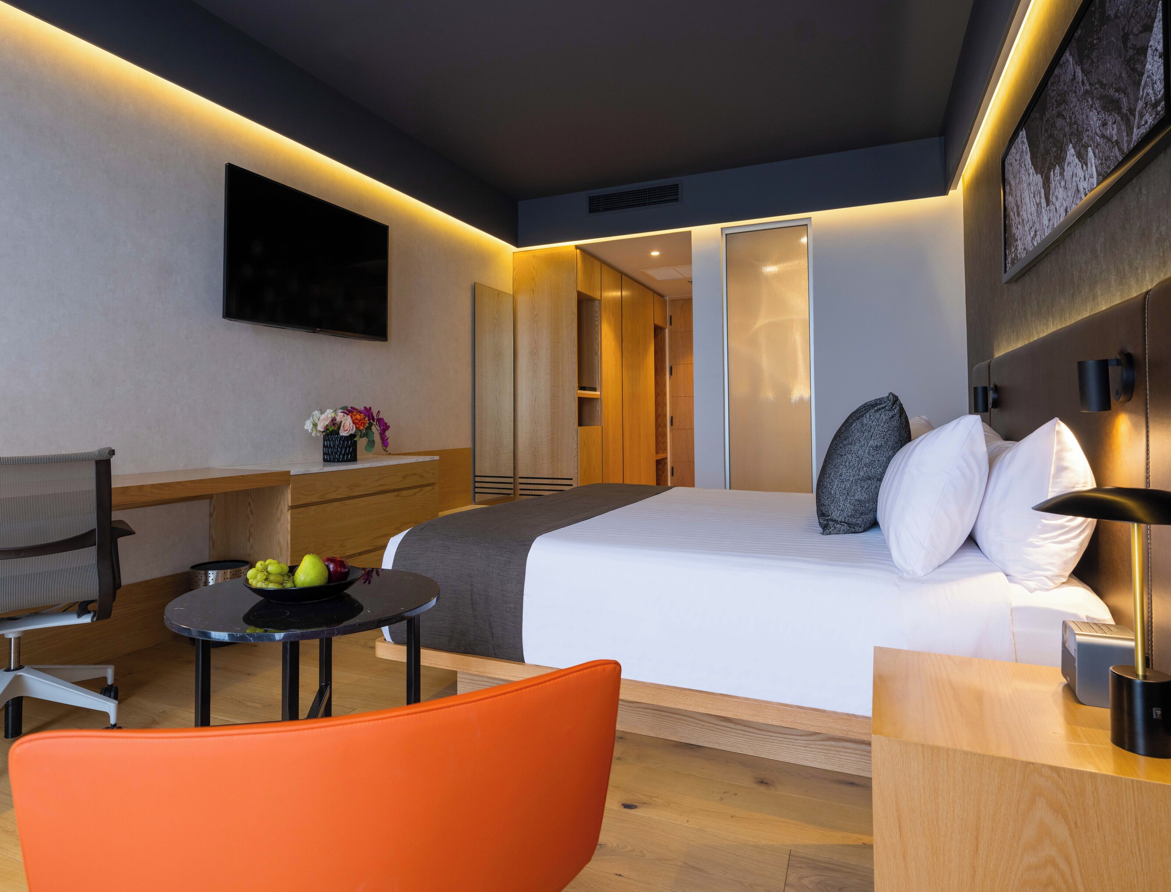 Una habitación de hotel moderna con una cama, un escritorio, una silla y una mesita con fruta.