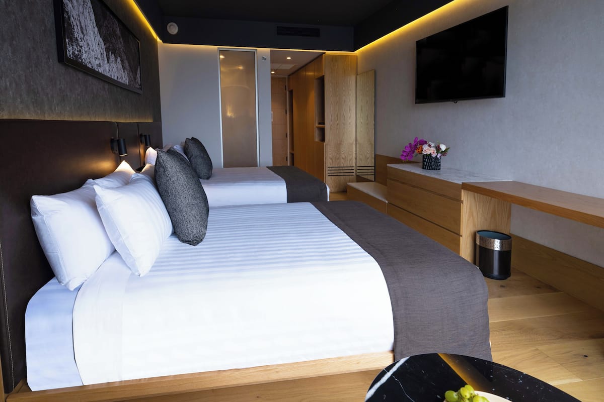 Une chambre d’hôtel moderne équipée de deux lits, d’un téléviseur à écran plat, d’un bureau en bois et d’une poubelle.