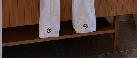 A modern bathroom with a wooden vanity, a large mirror, a white sink, and two towels hanging on hooks.