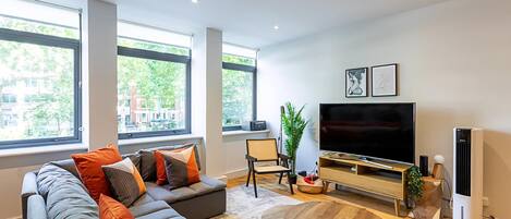 A modern living room with a sectional sofa, a flat-screen TV, a coffee table, and large windows.