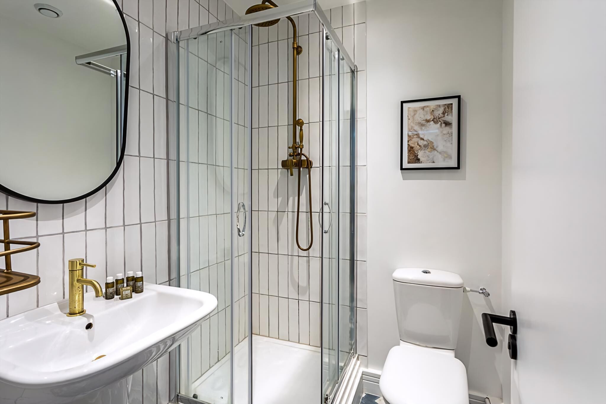 Een badkamer met een douchecabine van glas, een witte wastafel, een toilet en een ingelijst beeld aan de muur.