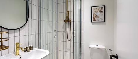 Een badkamer met een douchecabine van glas, een witte wastafel, een toilet en een ingelijst beeld aan de muur.