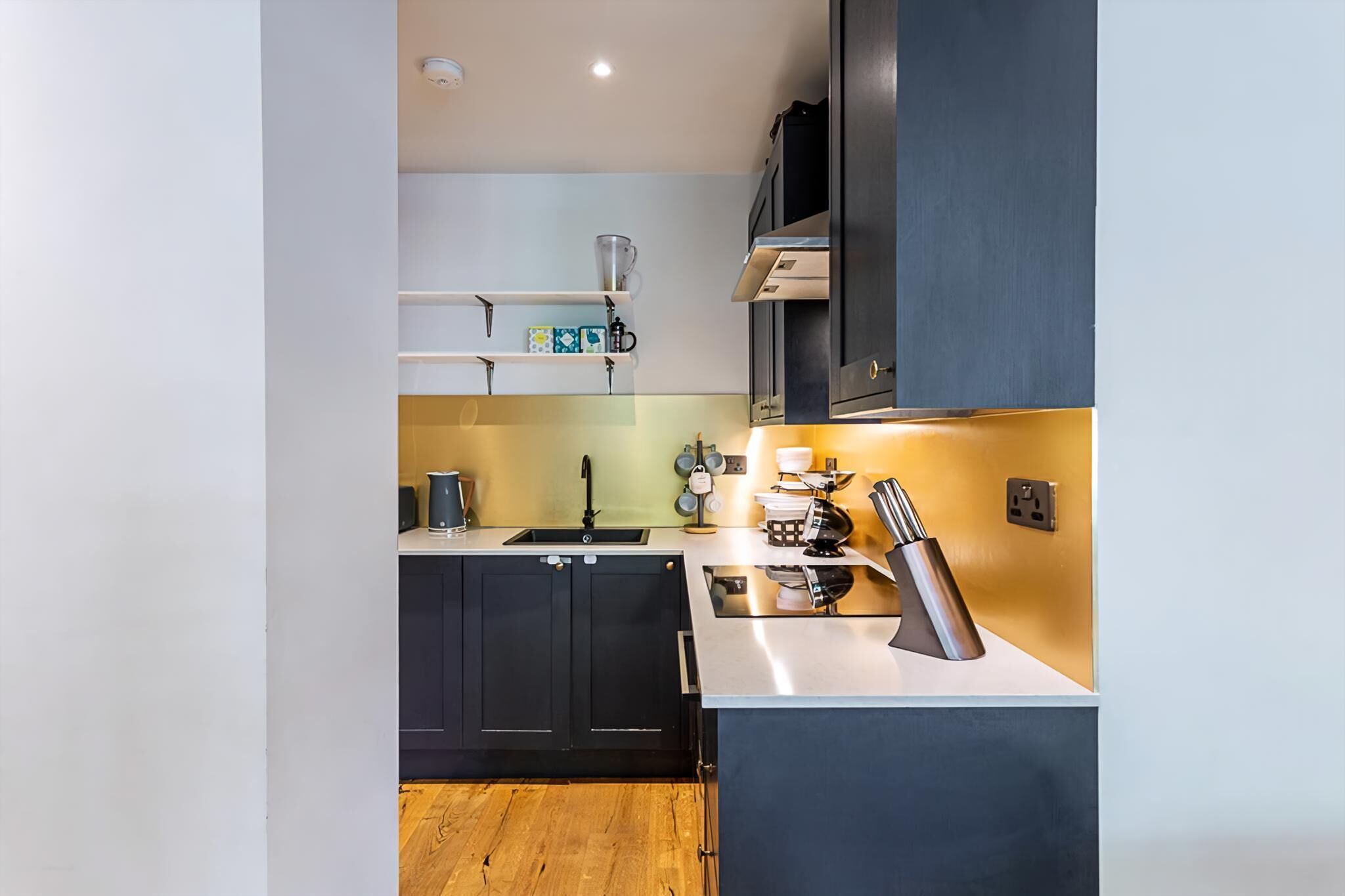 A modern kitchen with dark cabinets, a white countertop, and a stainless steel sink.
