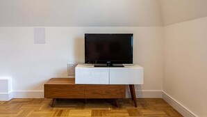 Ett modernt vardagsrum med en platt-TV placerad på en vit TV-bänk, trägolv och en inbyggd bänk.