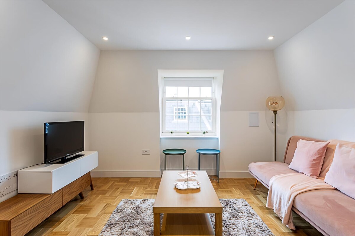 A modern living room with a flat-screen TV, a sofa, a coffee table, and two stools.