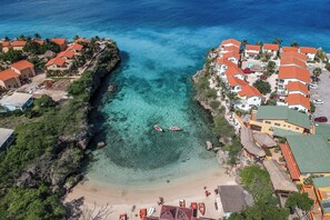 An aerial view of a coastal area with clear turquoise waters, a sandy beach, and buildings with red roofs. - Lovely apartment in resort close to beach. Beautiful bay. Swimming pool. (Lagun)