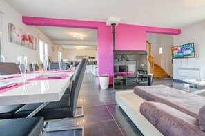 Ein modernes Wohnzimmer mit Essbereich, einer Couch, einem Fernseher und einer Treppe.