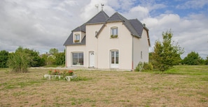 Ein zweistöckiges Haus mit einer symmetrischen Fassade, einem zentralen Eingang und einem kleinen Garten mit Blumen und Sträuchern.