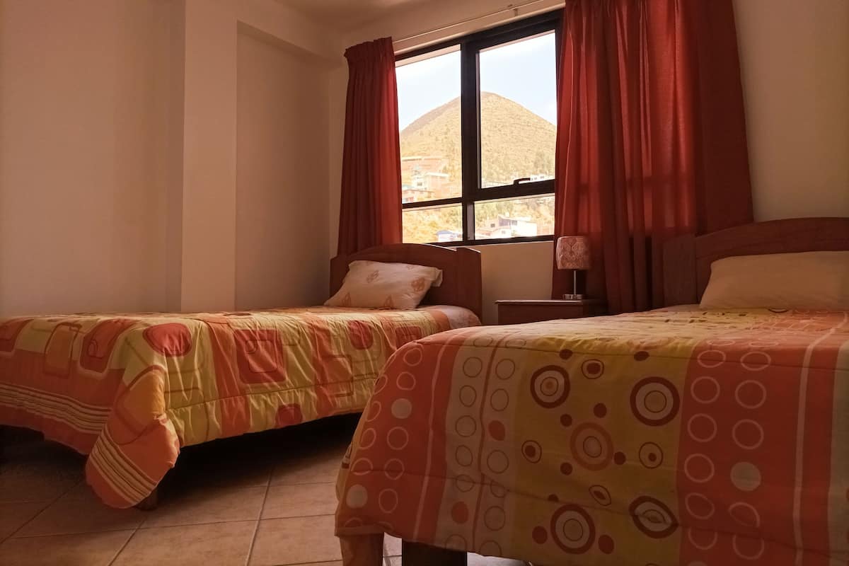 A hotel room with two beds, a window with curtains, a nightstand, and a lamp.
