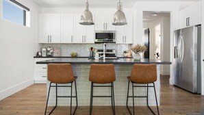 Una cocina moderna con armarios blancos, un refrigerador de acero inoxidable y una isla central con taburetes de bar.