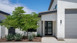 Un edificio moderno con una puerta de garaje, un árbol y plantas de agave en el jardín delantero.