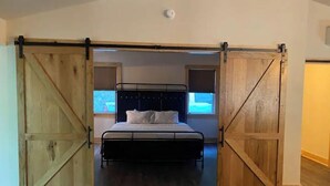 Une chambre à coucher avec un lit placé au centre, entre deux portes coulissantes de style rustique, une fenêtre au-dessus du lit et un luminaire au plafond.