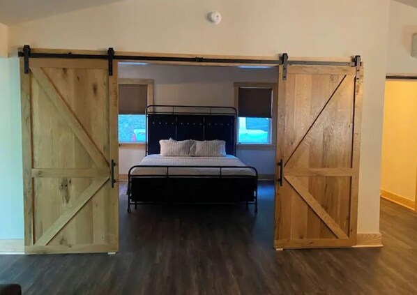 Quarto com uma cama centralizada entre duas portas de correr estilo celeiro, uma janela sobre a cama e um lustre no teto.