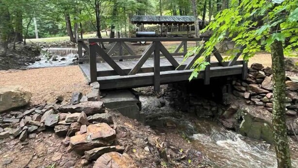 Un pont en bois enjambant un ruisseau, avec un abri rustique en arrière-plan.