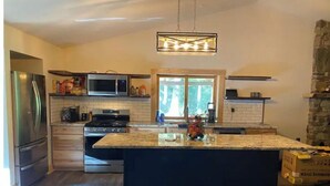 Une cuisine moderne dotée d’un îlot central, d’appareils électroménagers en acier inoxydable et d’un mur décoratif en pierre.