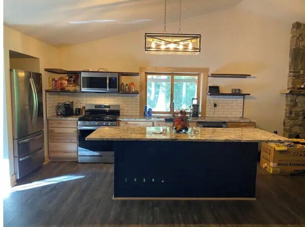 A modern kitchen with a central island, stainless steel appliances, and a stone accent wall. - Bear Den Cottage (Vesuvius)
