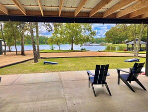 Un área de estar al aire libre con sillas y una mesa, con vista a un lago con barcos y un césped.