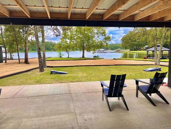 An outdoor seating area with chairs and a table, overlooking a lake with boats and a grassy area.