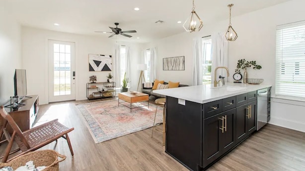 Un salón amplio con cocina central grande, piso de madera y ventilador de techo.