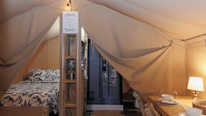 A tented accommodation with a bed, a table with bowls, and a lamp. - BEARADISE “Glamping Paradise” (Vesuvius)