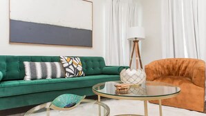 Ein Wohnzimmer mit einem grünen Sofa, einem runden Glastisch und einem orangefarbenen Sessel.
