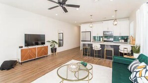 Ein modernes Wohnzimmer mit Fernseher, Sofa und Couchtisch. Es gibt eine Küchenzeile mit Bar und Barhocker.