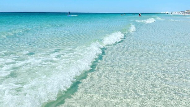 Una playa con agua turquesa cristalina, algunas personas y una costa distante con edificios.